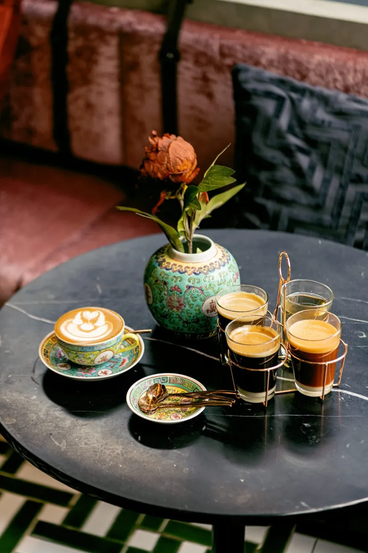 Coffee, espresso glasses and a small vase set out on a dark marble table at TAMP Kafei and BAR
