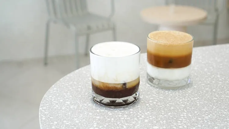 Two layered coffee drinks in glasses on a terrazzo table at PAGA Microroastery
