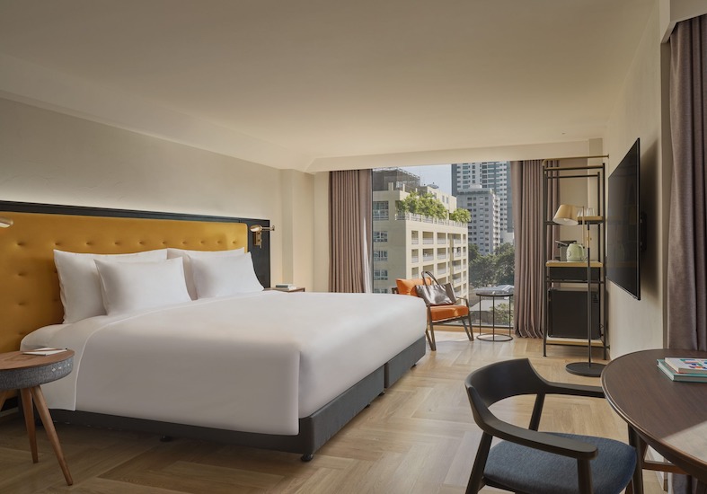 King bed with a mustard headboard, a wall-mounted television and a window onto the city