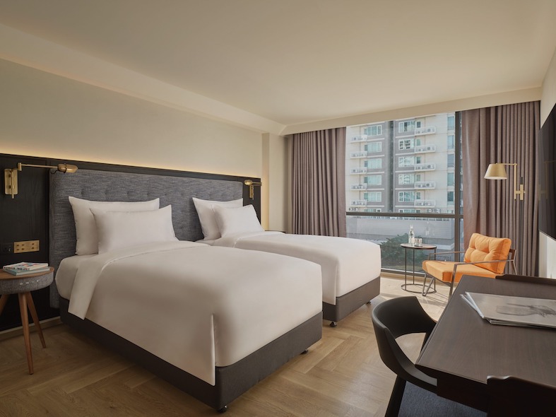 Uptown Room laid out with twin beds, an orange armchair and a city view over Sukhumvit