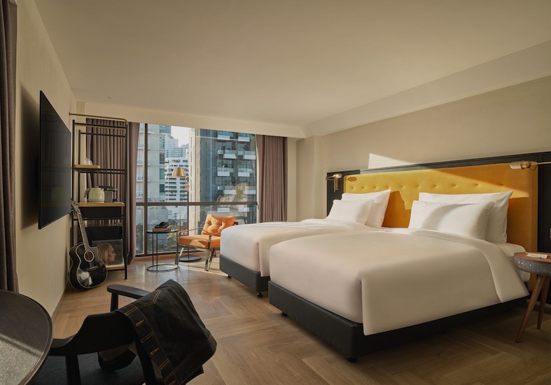 Twin beds with a yellow headboard, open shelving and a window over the neighbourhood