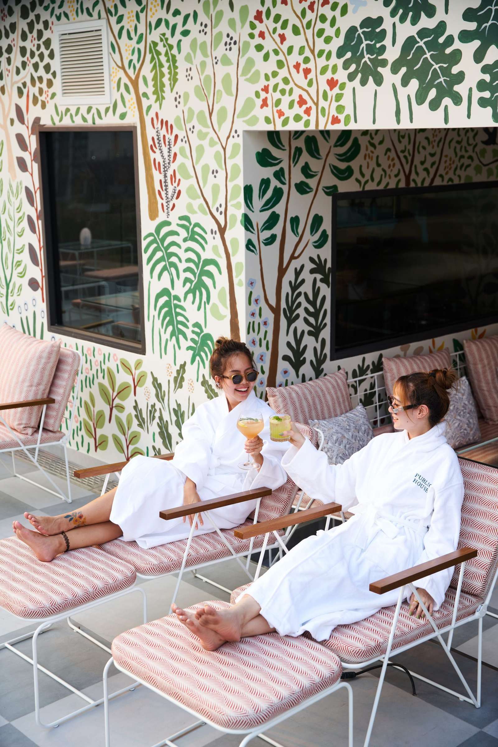 Two guests in robes with drinks on the botanical-papered terrace at Public House Bangkok