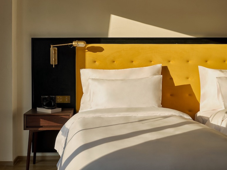 Bed with a buttoned yellow headboard and a timber bedside table