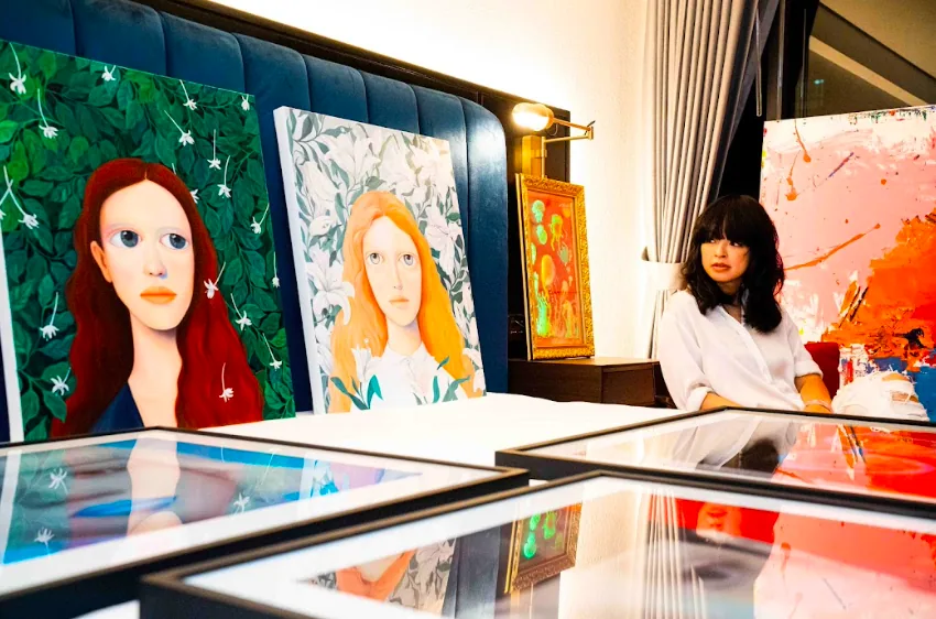 An artist at work beside painted portraits at an art fair booth in Bangkok