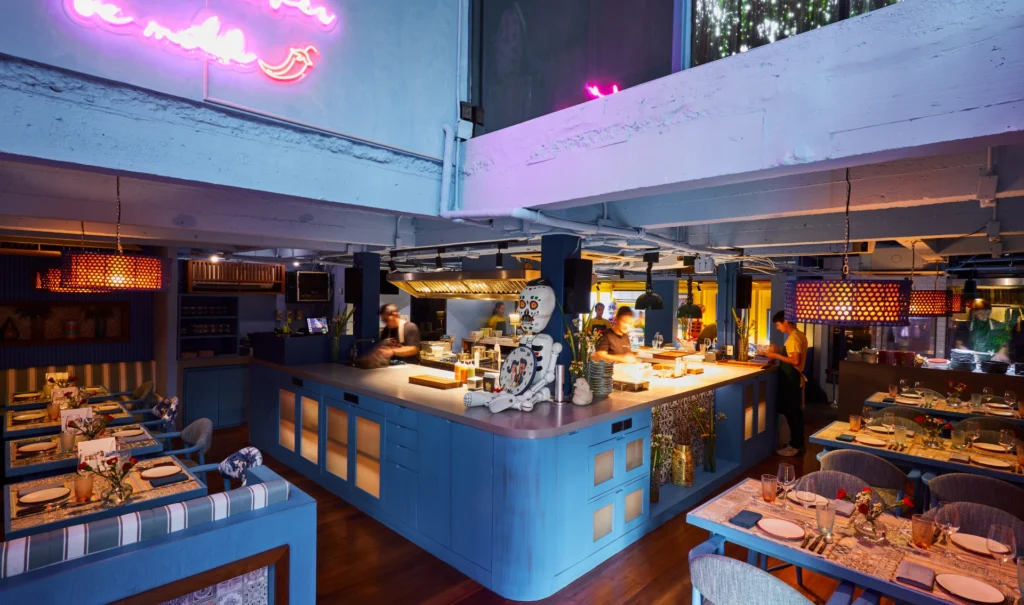 A Bangkok dining room with blue banquettes and an open kitchen behind