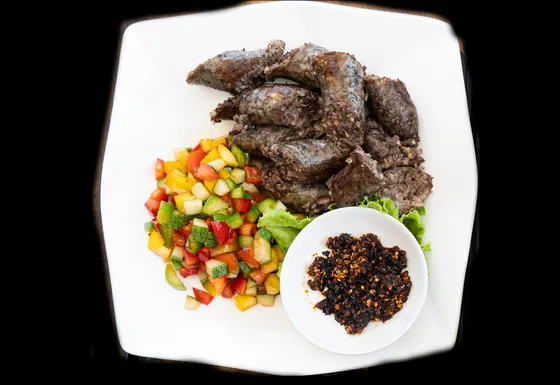 Grilled beef with chopped vegetables and a chilli dip on a white plate