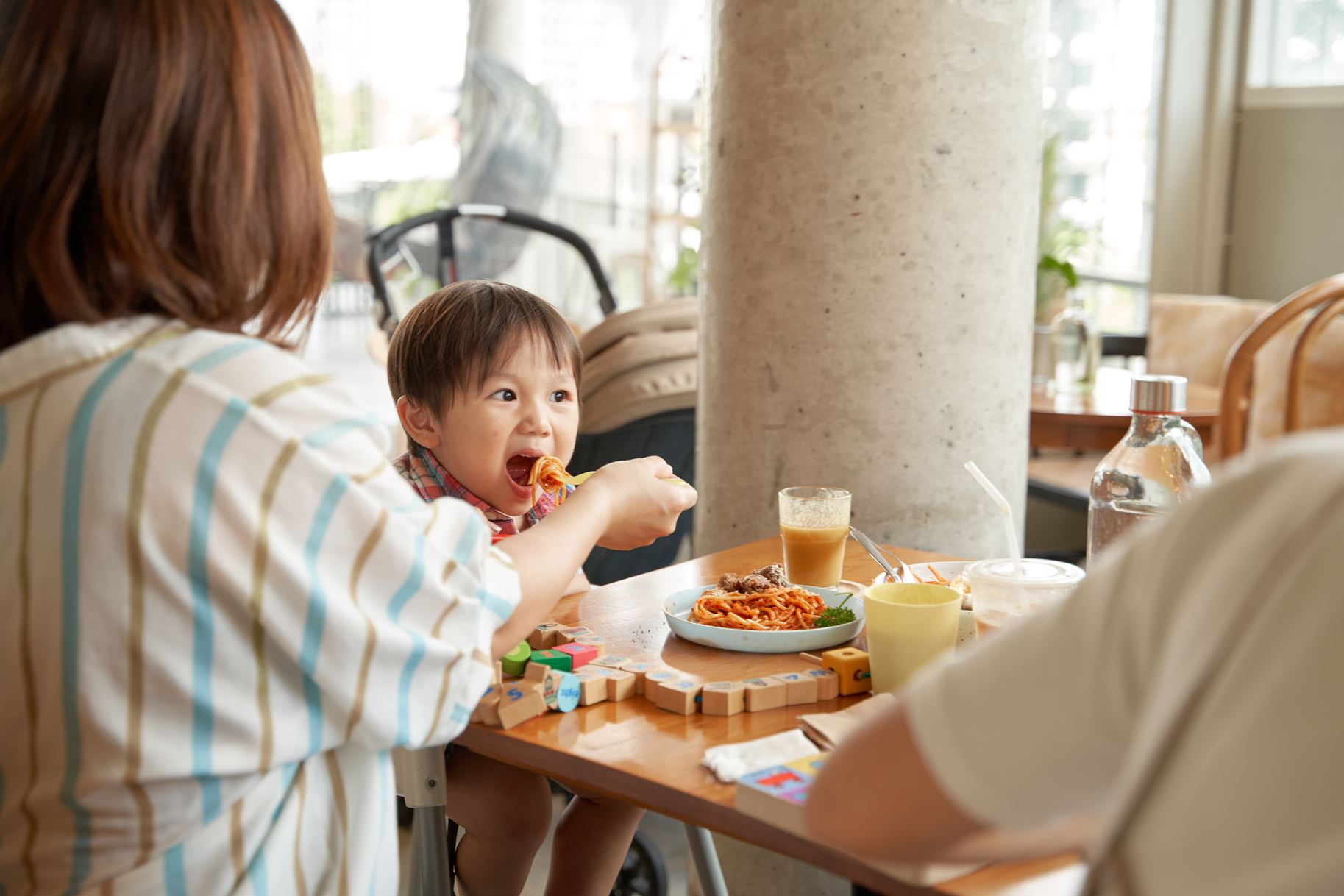 A small child eating at a café table with a parent