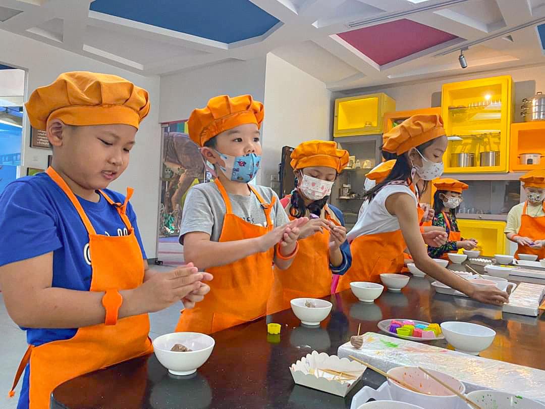 Children in aprons and chefs’ hats at a Bangkok cooking class