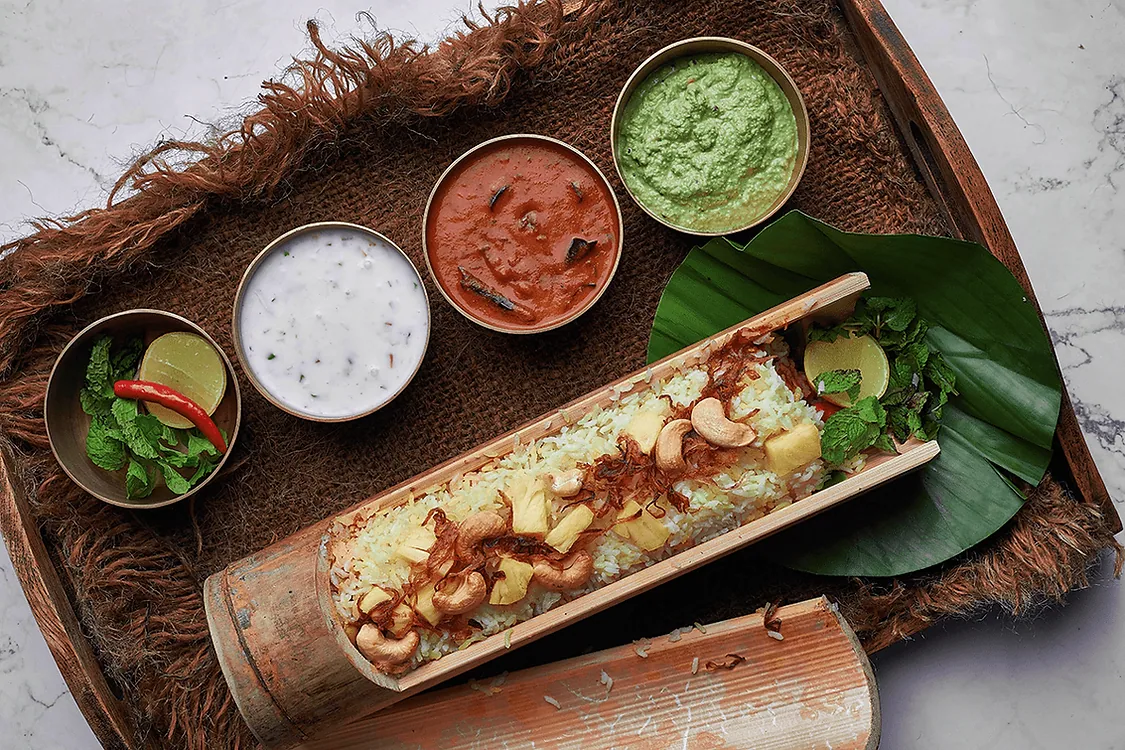 A grilled bamboo-tube dish served with three dips on a woven tray