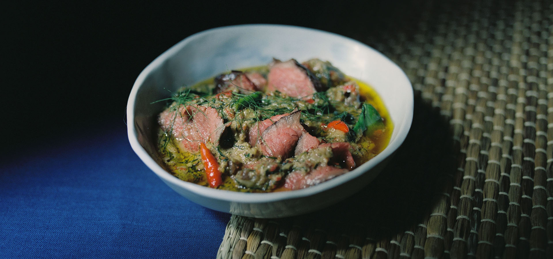 A bowl of sliced beef in a green herb sauce