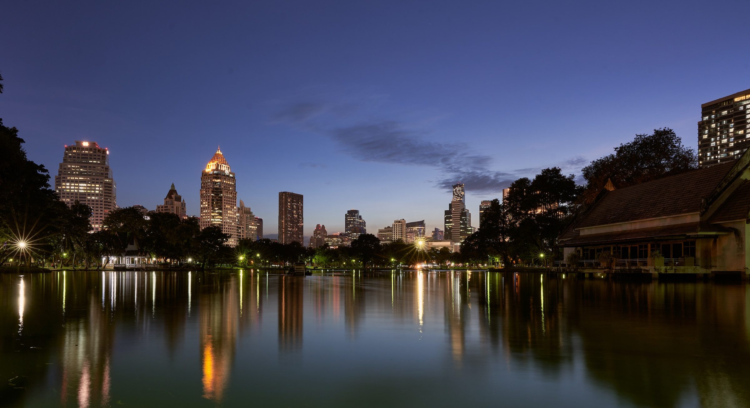 A park lake at dusk reflecting the lit Bangkok skyline