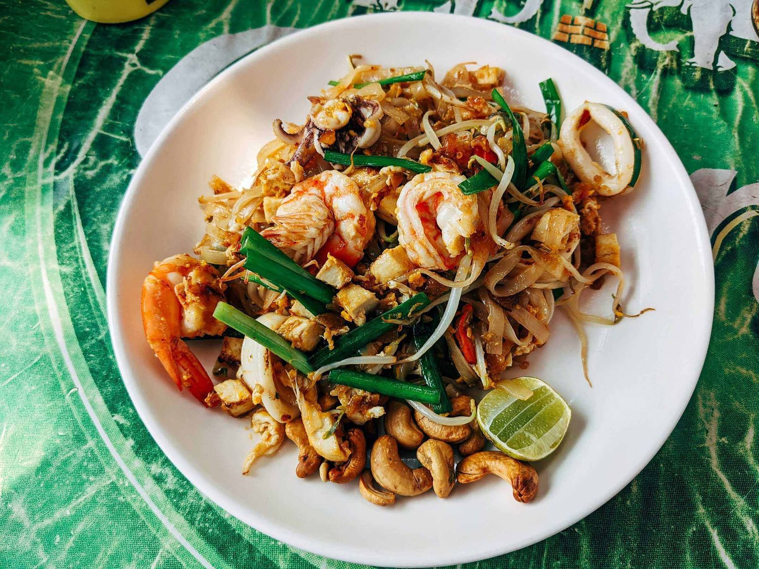 A plate of pad thai with prawns and a wedge of lime