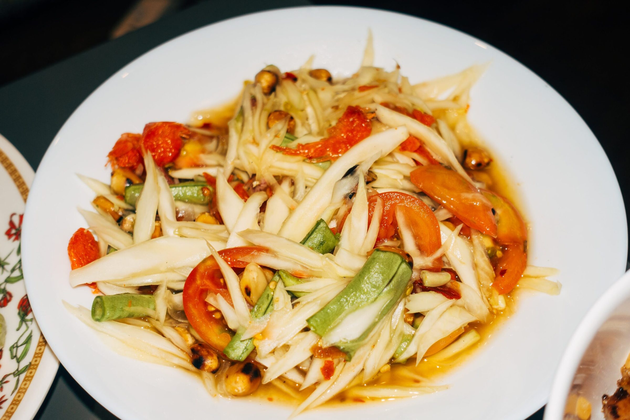 A plate of som tam, green papaya salad, with tomato and long beans