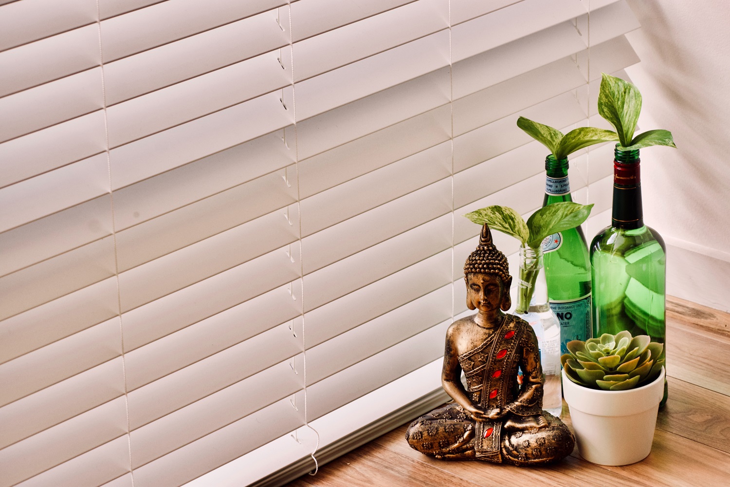 A small brass Buddha figure, potted plants and bottles on a sunlit sill
