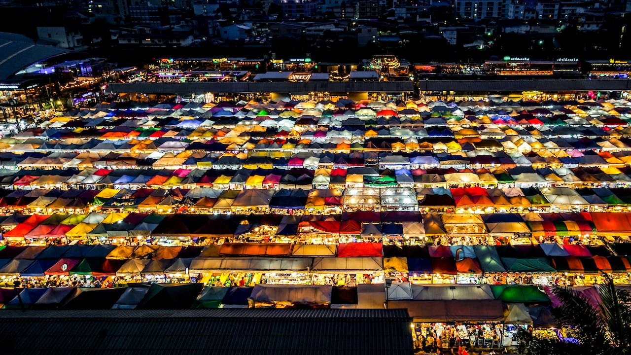 The lit stall roofs of a Bangkok night market seen from above