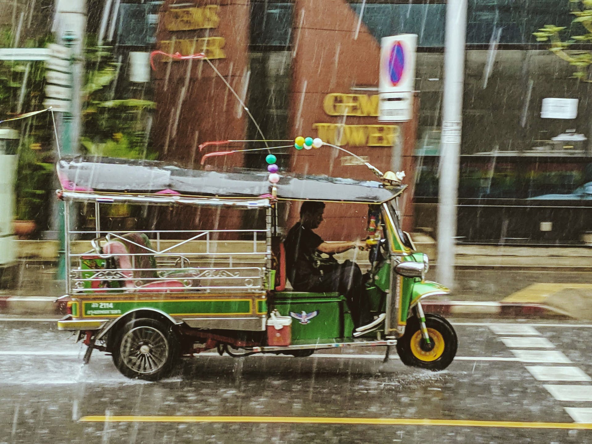 A green tuk-tuk parked in the rain on a Bangkok street