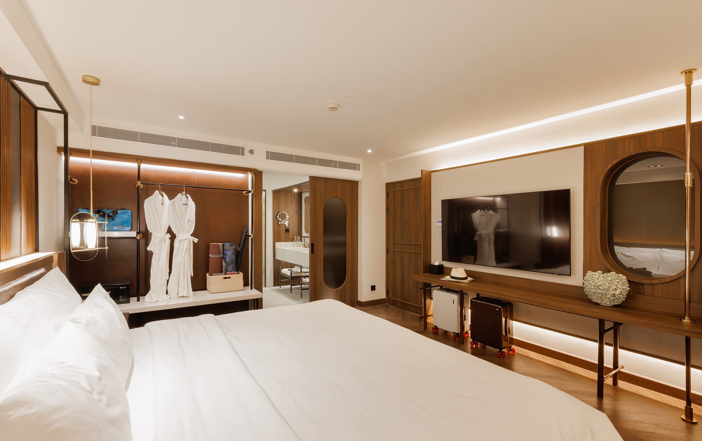 Bedroom with an open wardrobe hung with robes, facing a media wall