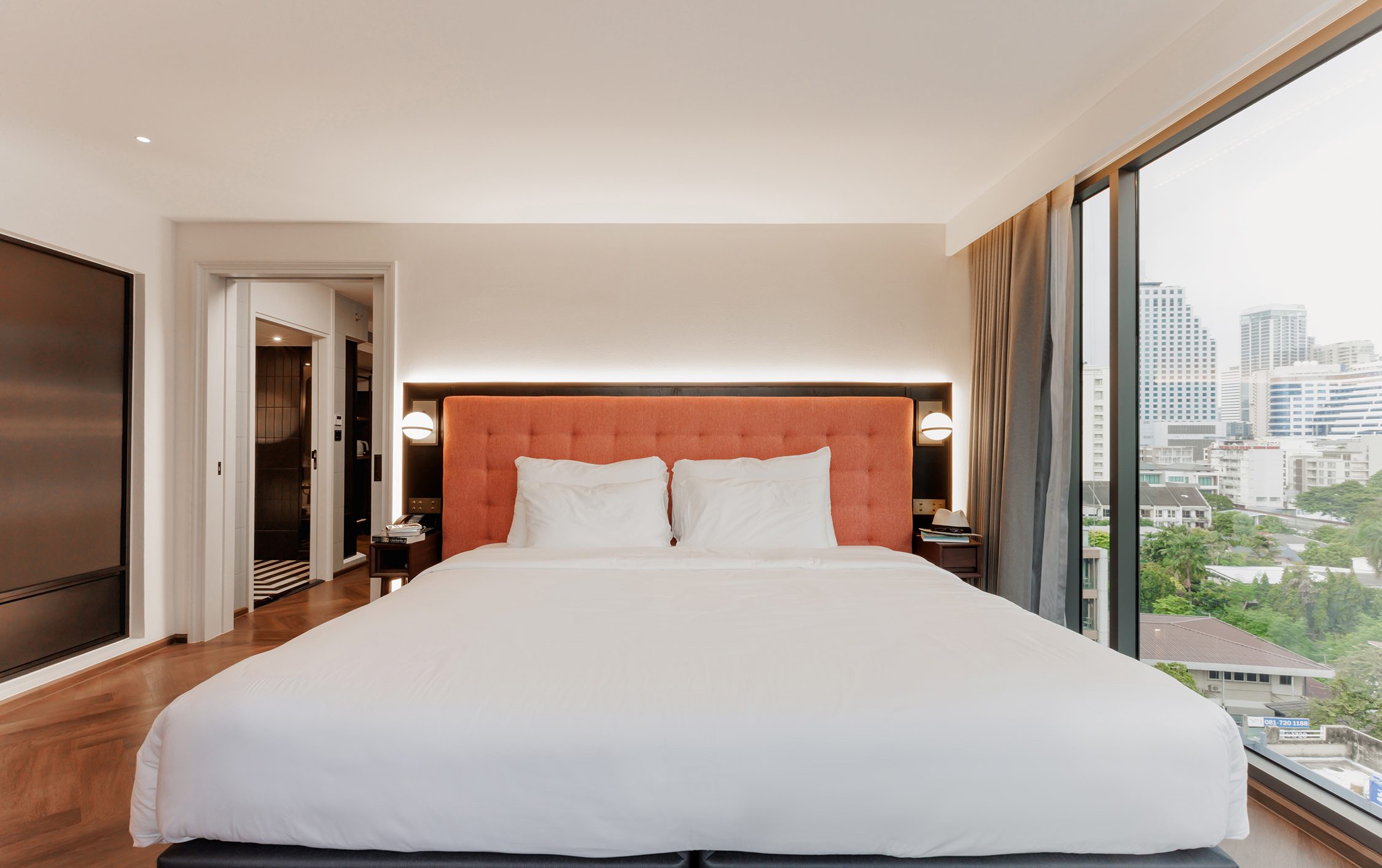 Bed with a terracotta headboard set between two windows over the city