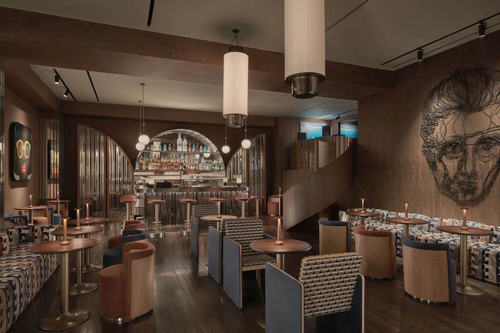 The bar at Public House Bangkok, with round tables and stools in front of the arched bottle wall