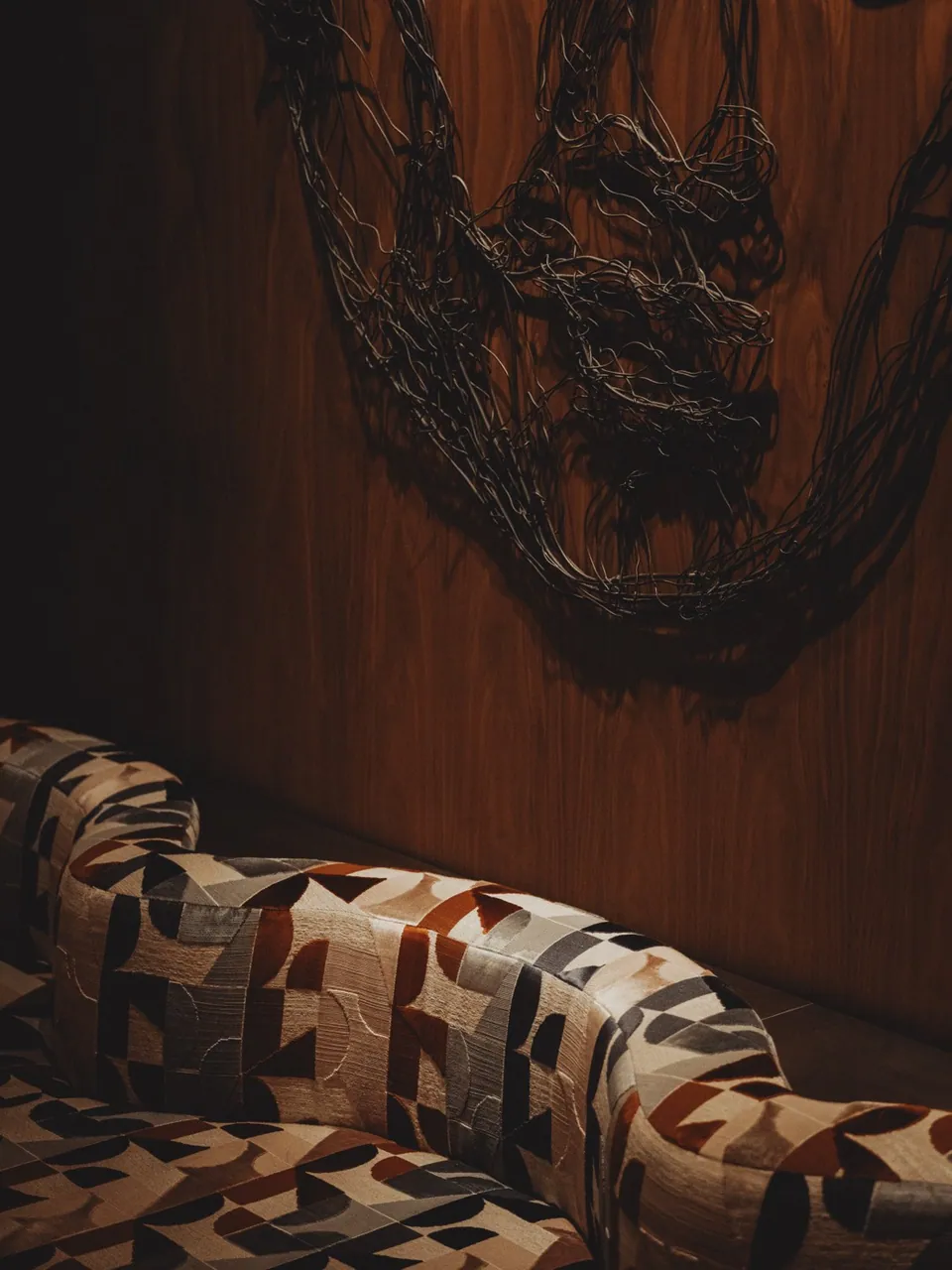 A patterned banquette below the wire-drawn portrait in the bar at Public House Bangkok