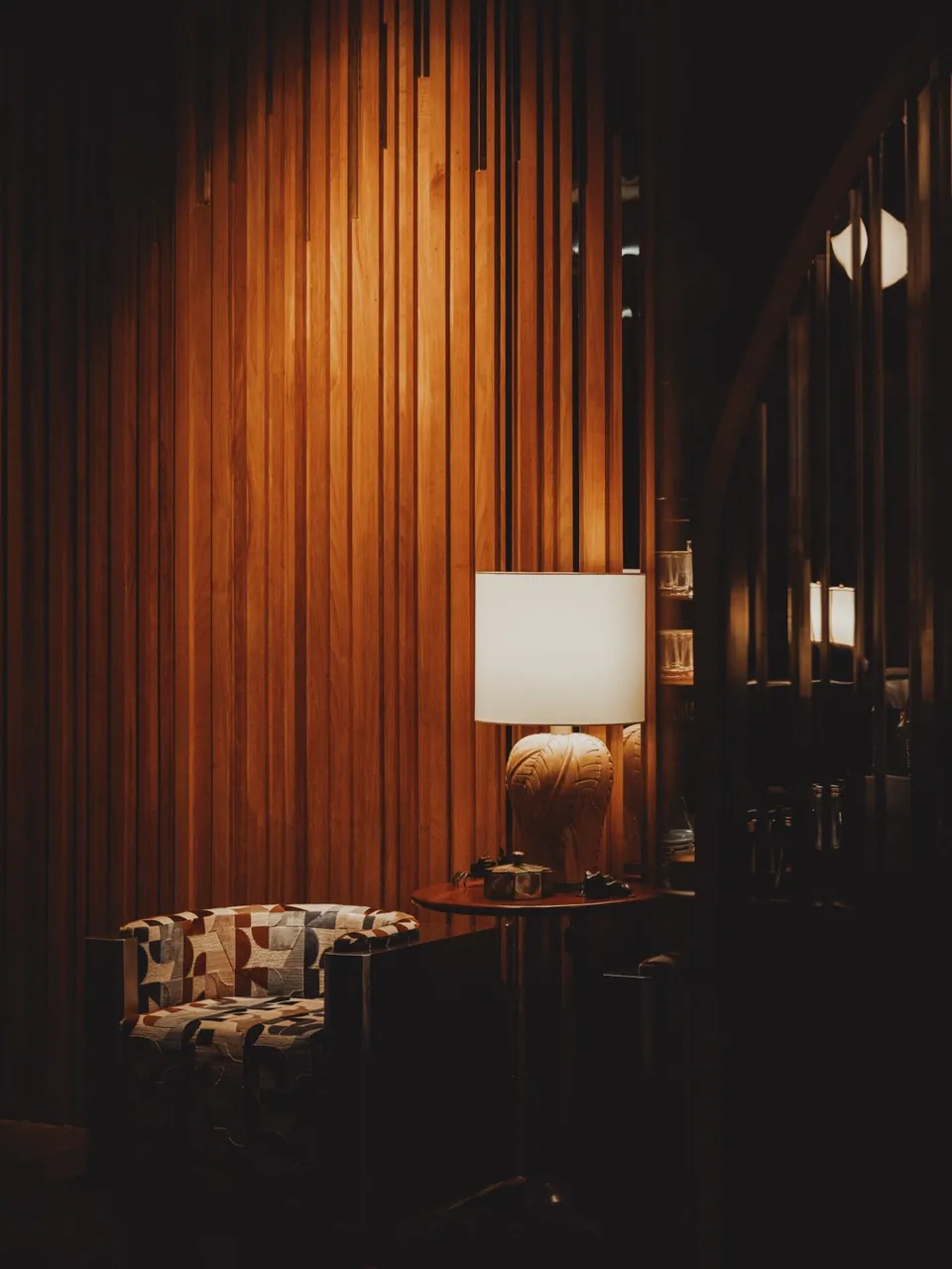 A lamp-lit corner of the lounge at Public House Bangkok, against a warm timber screen