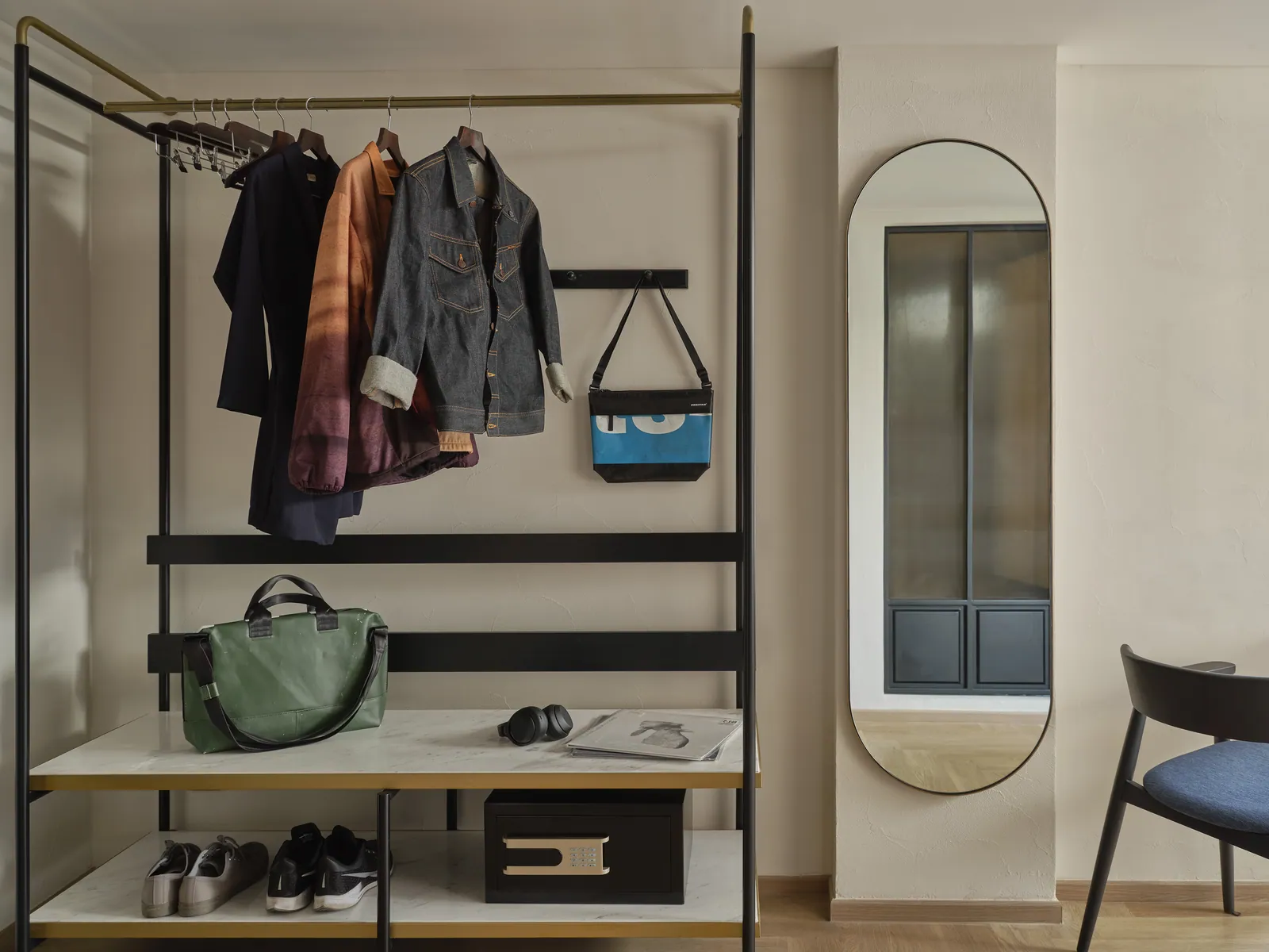 An open wardrobe hung with clothes and a bag beside the desk of a guest room at Public House Bangkok