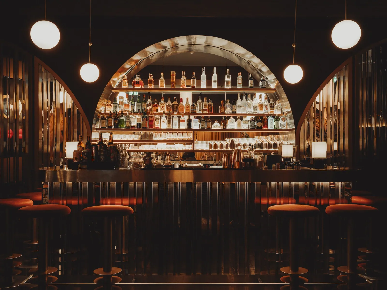 The arched back bar at Public House Bangkok, lined with bottles above a row of leather stools