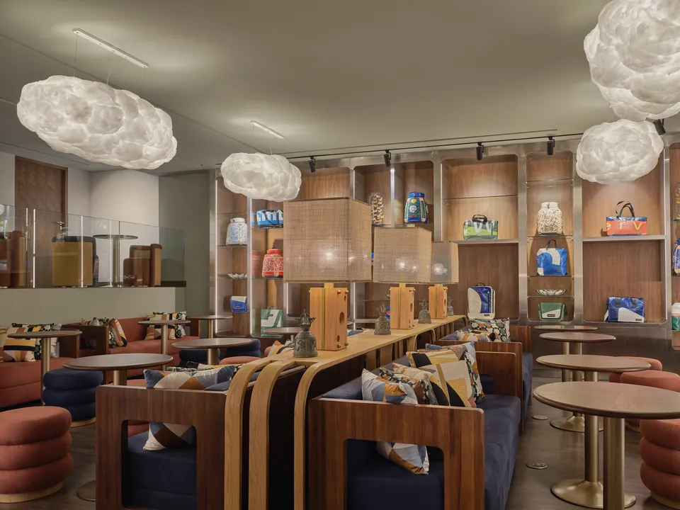 The long shared work table in FORUM at Public House Bangkok, under cloud-shaped pendant lights and shelves of books and objects