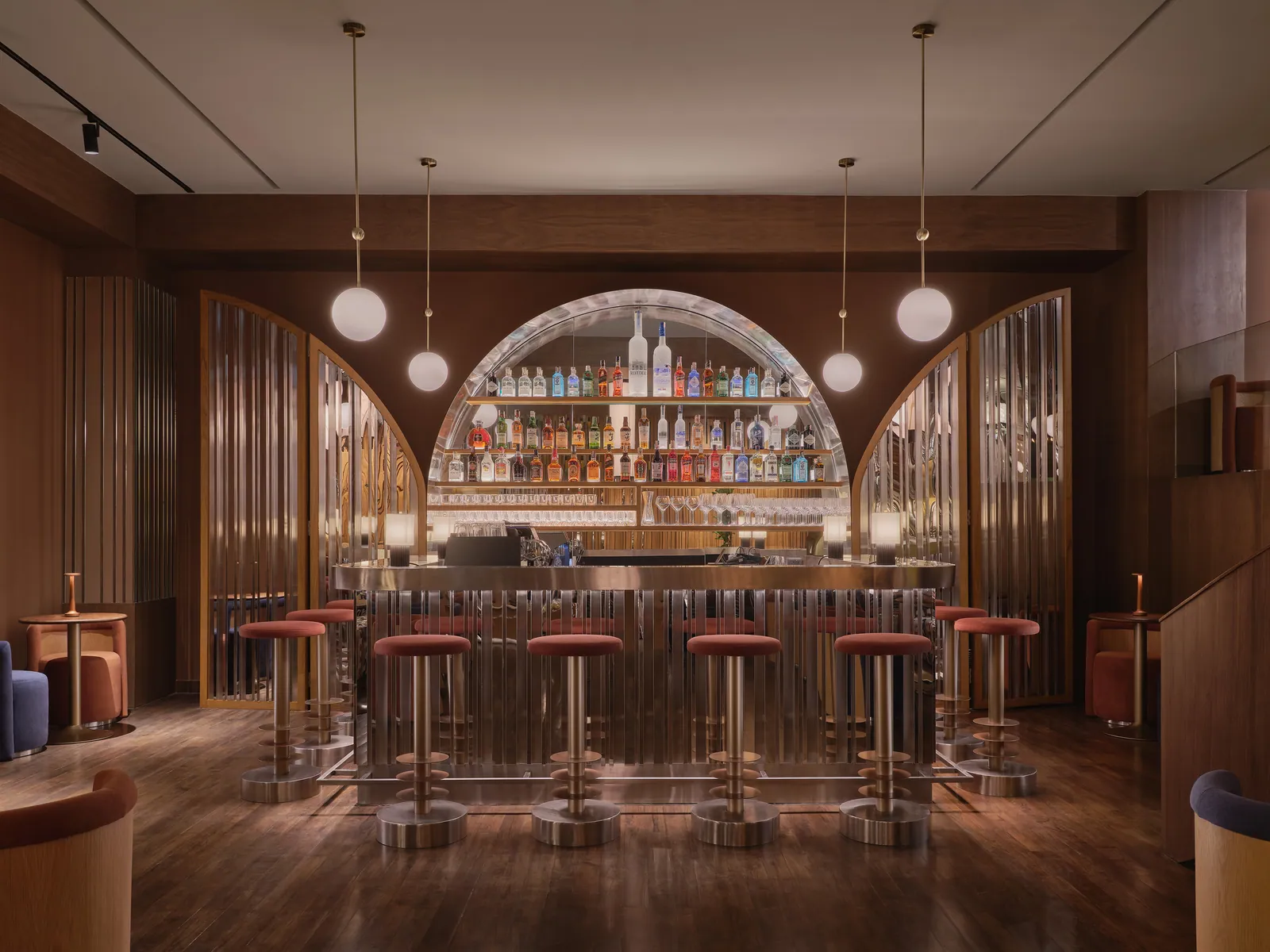 The bar at Public House Bangkok, with an arched bottle wall, globe lights and a row of stools along the counter