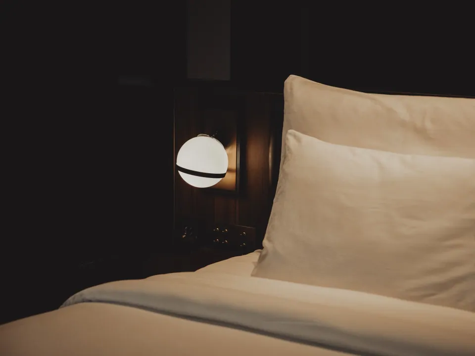 A guest room at Public House Bangkok at night, lit by a single pendant beside the bed