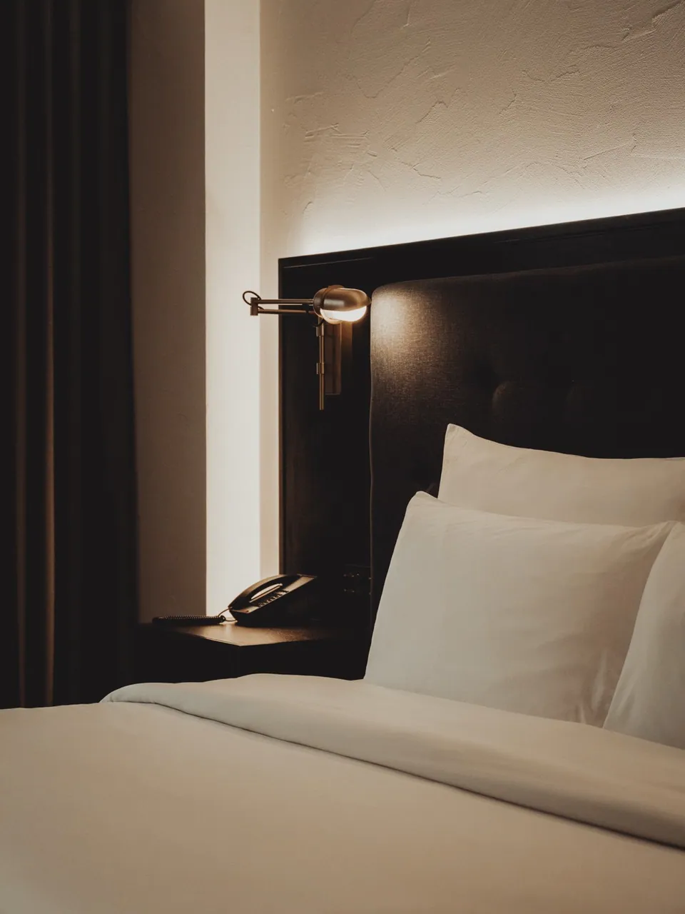 A reading lamp beside the bed in a guest room at Public House Bangkok, behind a timber screen