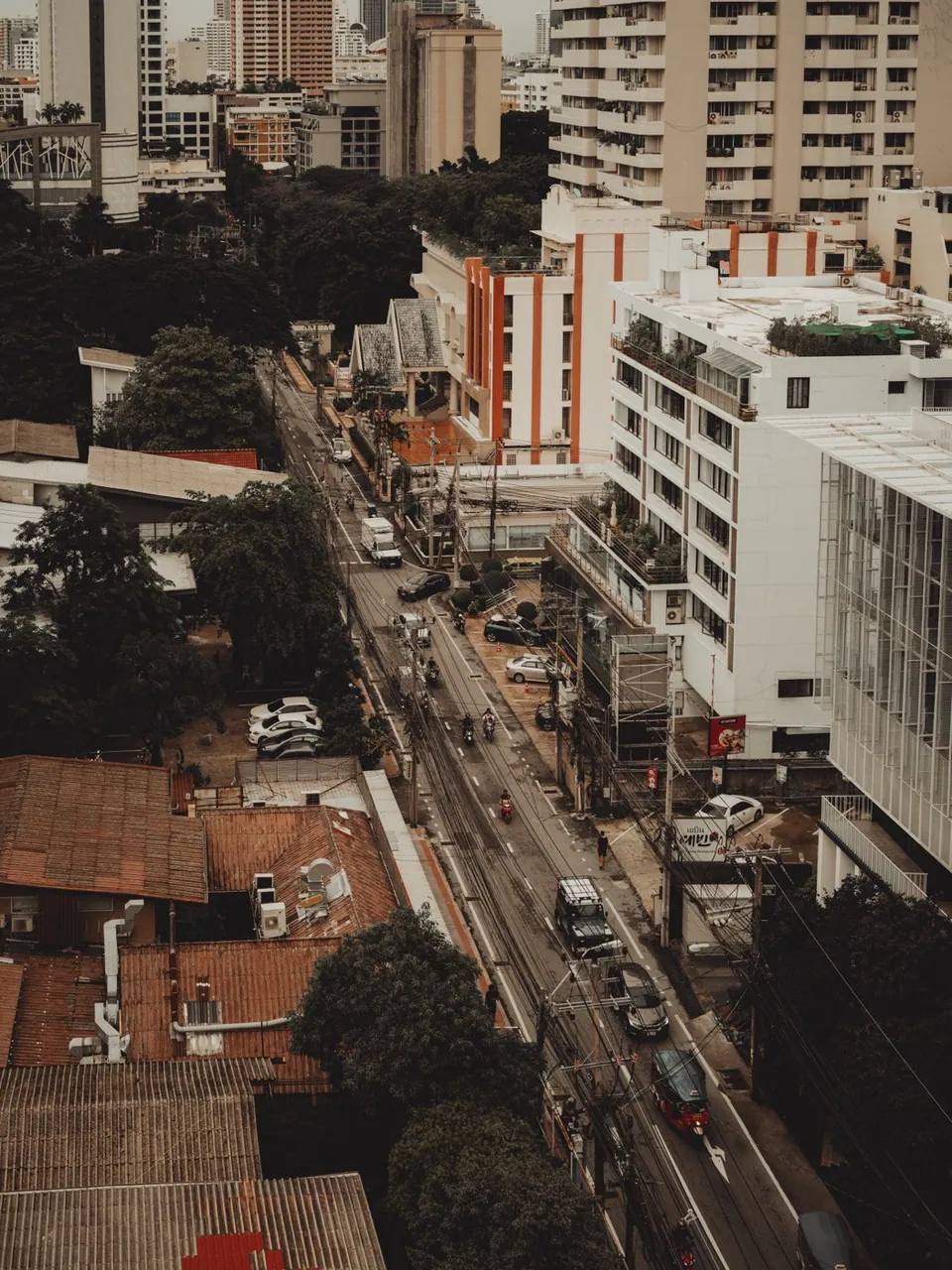 Looking down over a Sukhumvit soi in Bangkok, with tiled roofs, trees and traffic between low-rise buildings