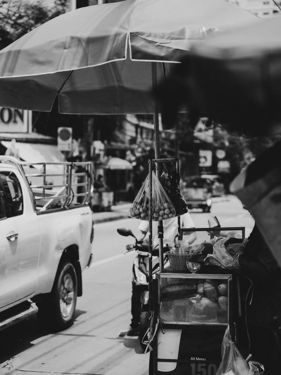 A street fruit cart under a parasol beside traffic in the Sukhumvit neighbourhood of Bangkok
