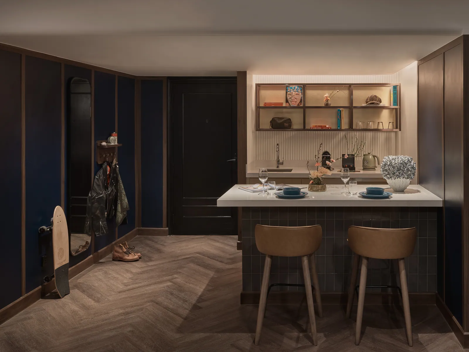 A suite kitchen and dining table at Public House Bangkok, laid under a lit shelf of glassware