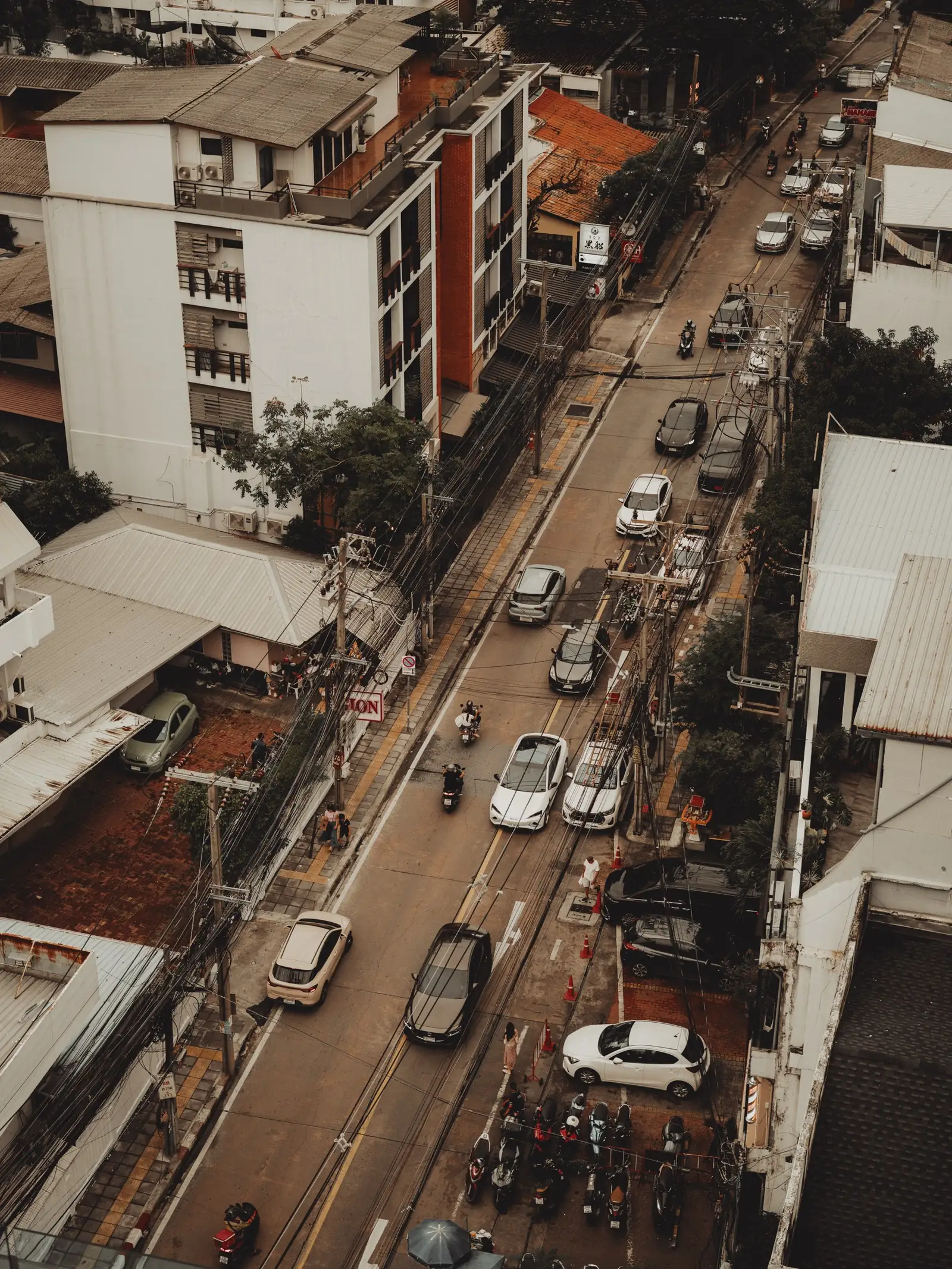 The soi below Public House Bangkok seen from above, cars and motorbikes on the road between the shophouses