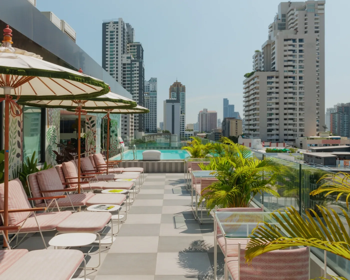 Paper parasols over striped loungers beside the rooftop pool at THE MOOON, Public House Bangkok, with the Sukhumvit skyline behind