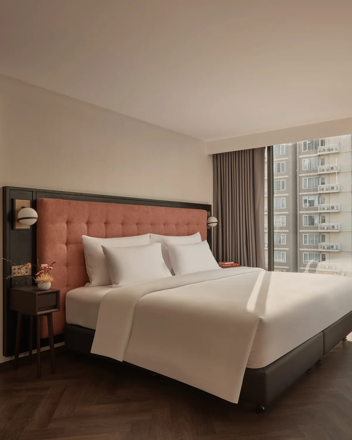 A king bed with a terracotta tufted headboard and a reading light in a guest room at Public House Bangkok