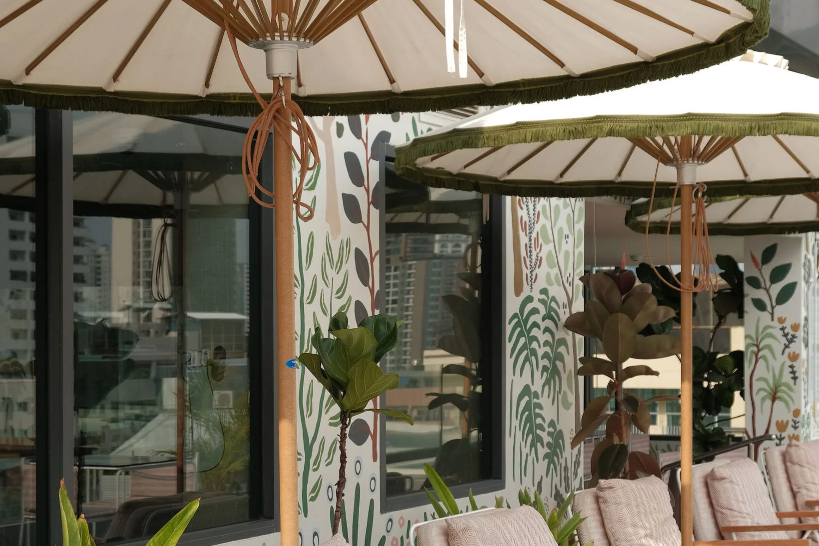 Thai parasols shading striped loungers on the rooftop deck at Public House Bangkok, beside the painted botanical mural