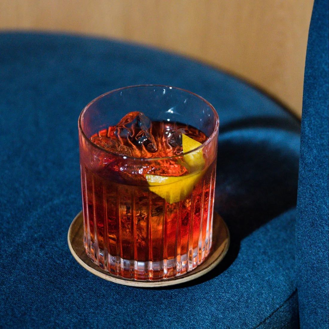 A cocktail served over ice on a blue velvet seat at Public House Bangkok
