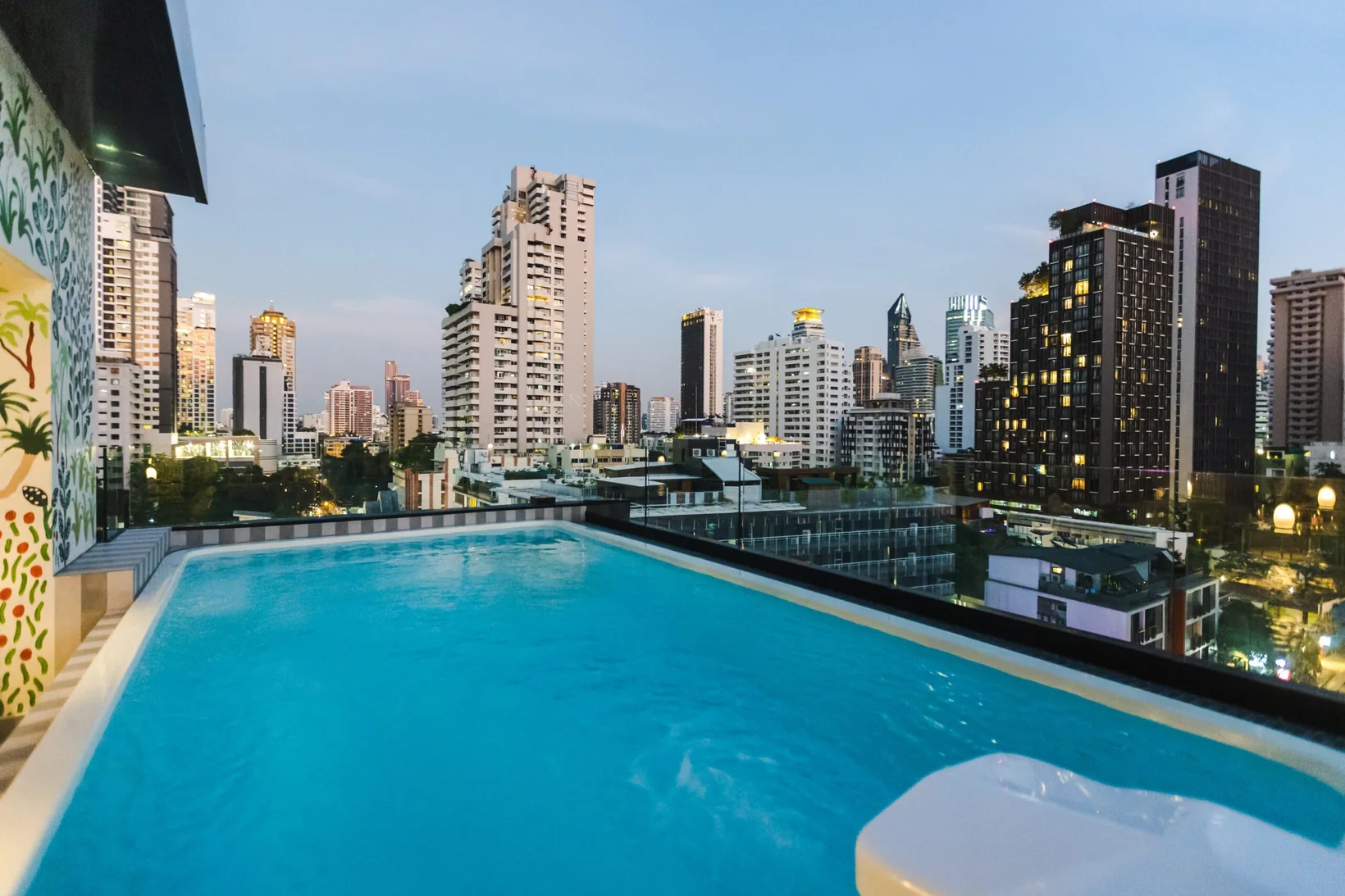 The rooftop swimming pool at Public House Bangkok at dusk, looking out over the Sukhumvit skyline