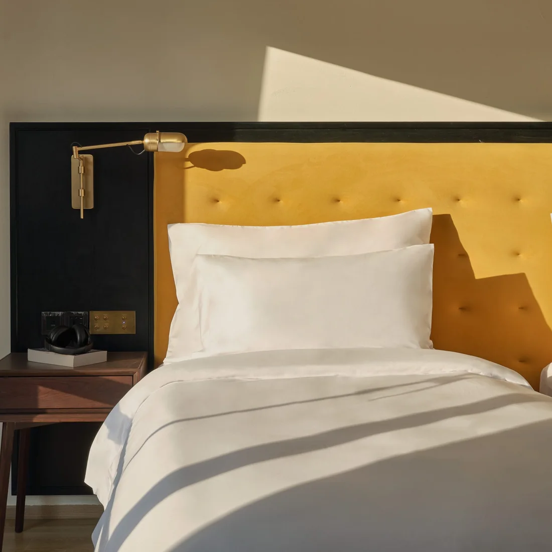 A guest room bed at Public House Bangkok, with a yellow tufted headboard
