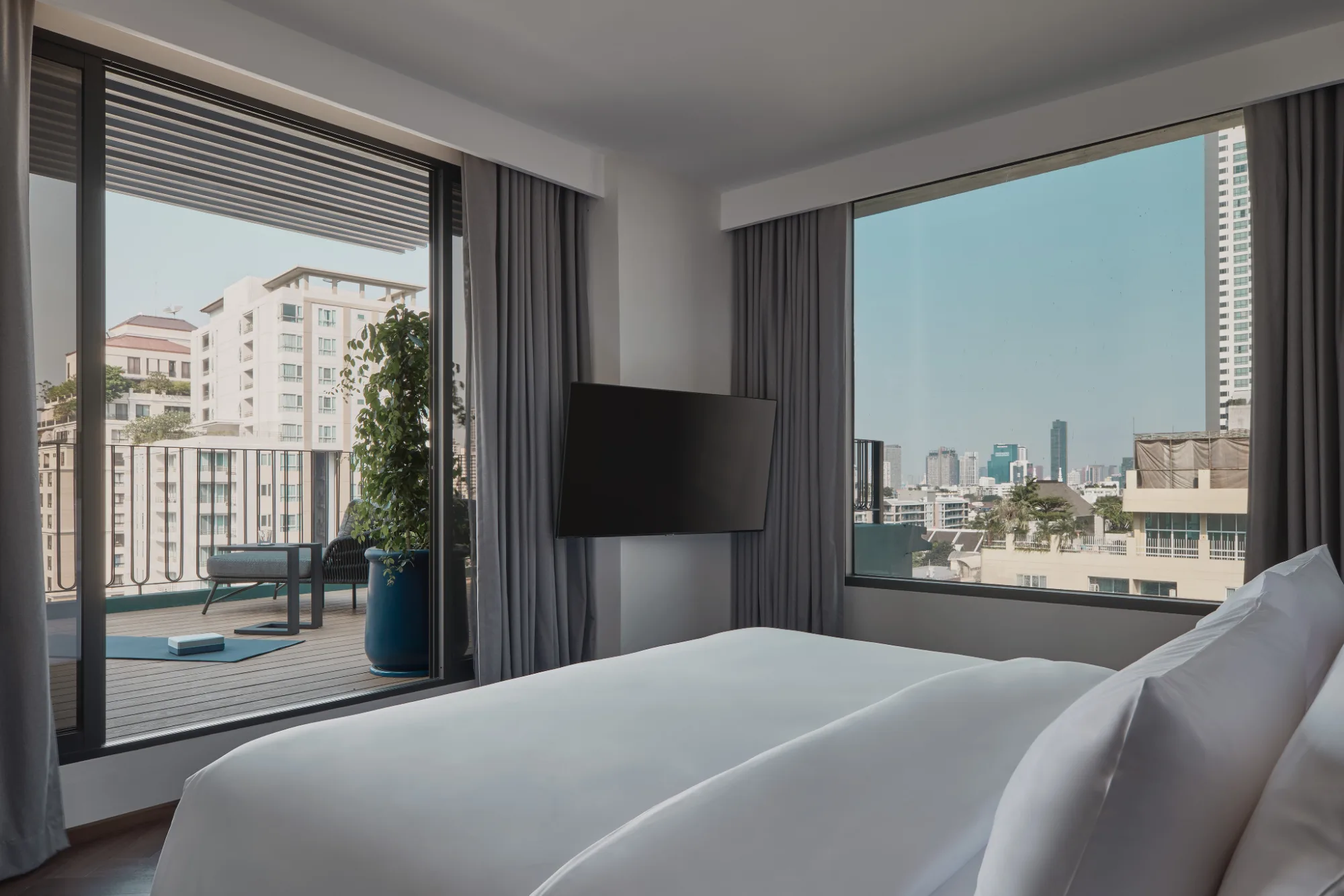 A made bed beside a floor-to-ceiling window looking over the Sukhumvit skyline at Public House Bangkok