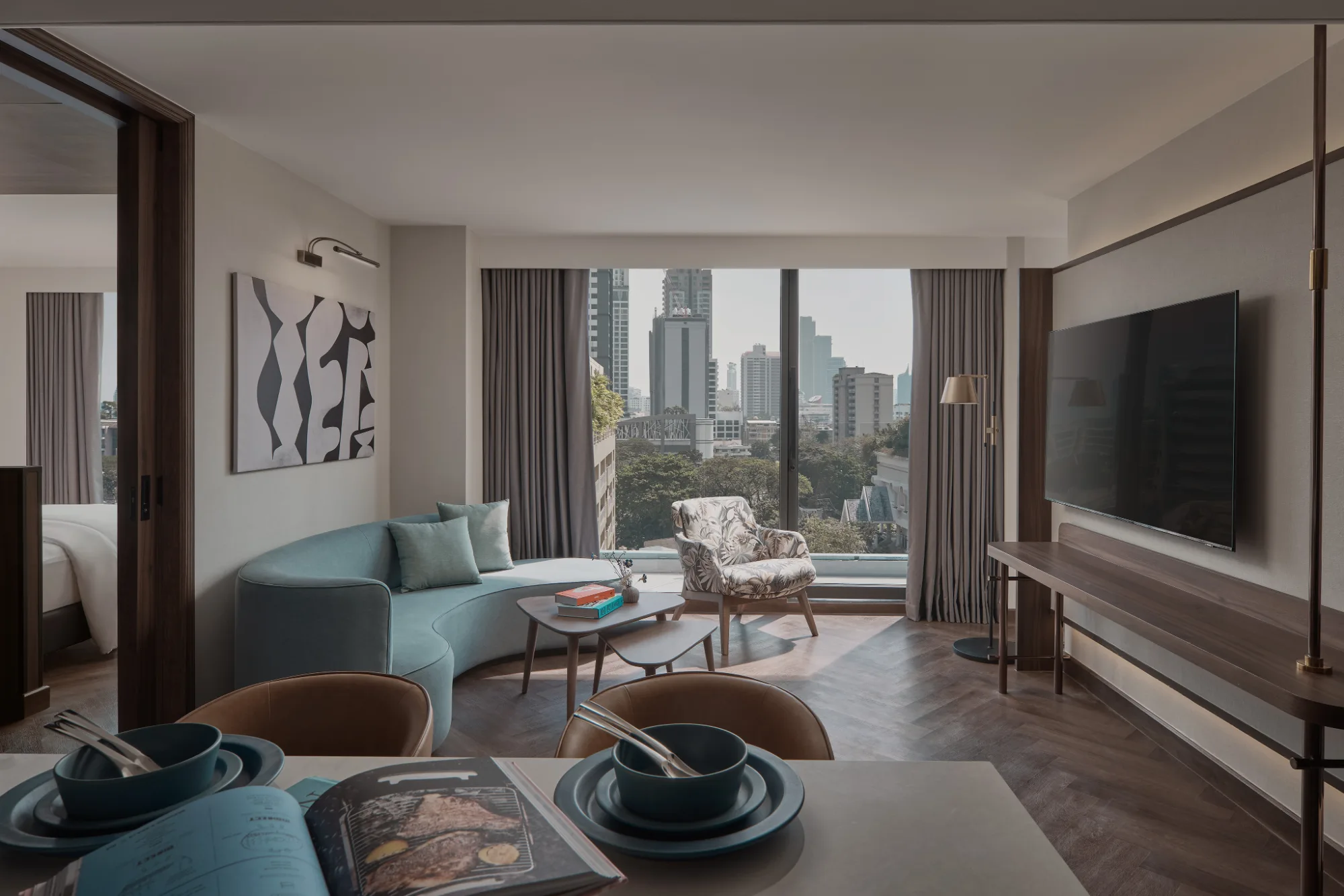 The living area of a suite at Public House Bangkok, a sofa and low tables in front of the city window