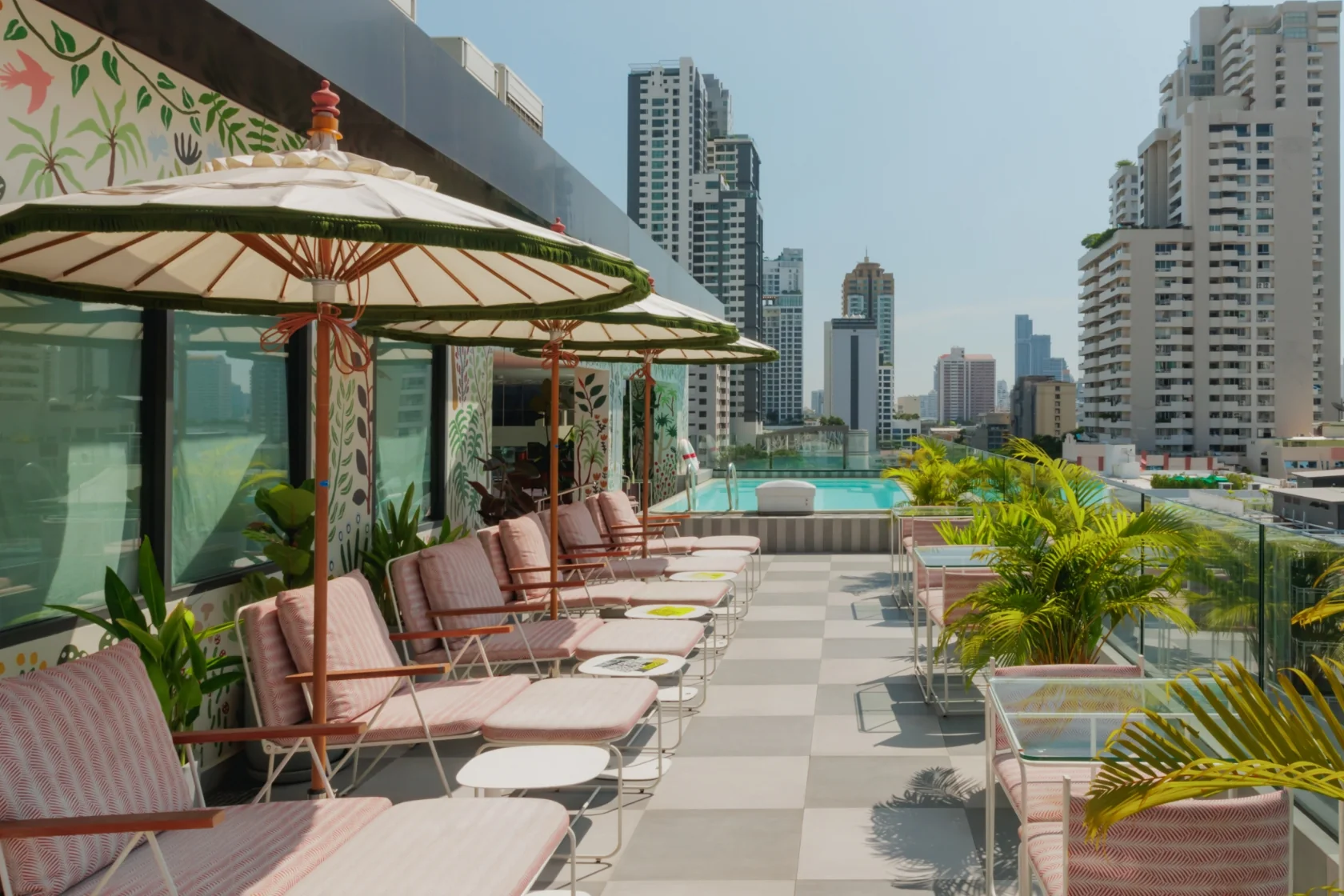 Paper parasols over striped sun loungers on the rooftop at THE MOOON, the swimming pool and the Sukhumvit skyline beyond