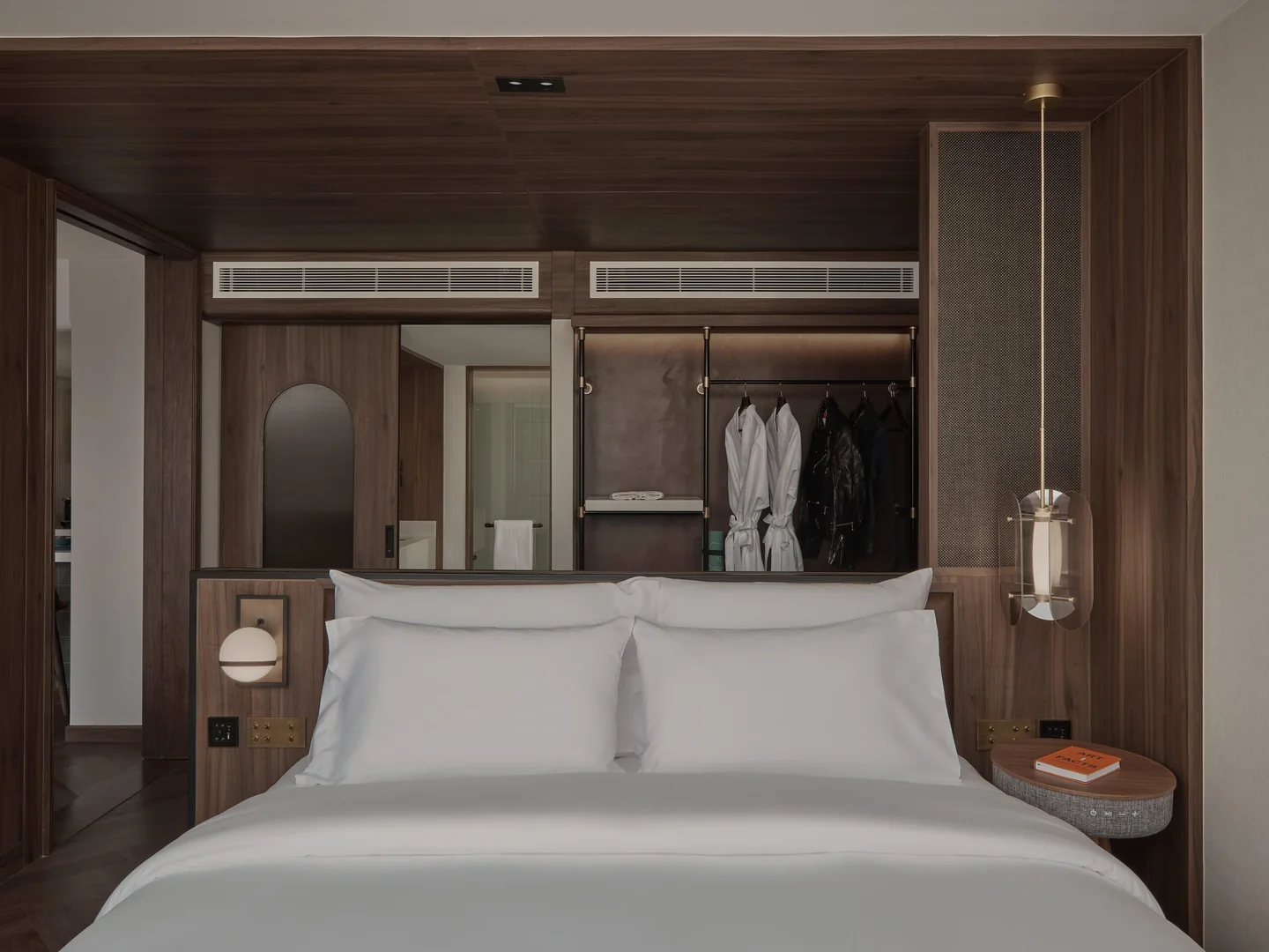 The bed of the 62 sqm Executive Suite at Public House Bangkok, framed by a walnut wardrobe and a glass pendant lamp