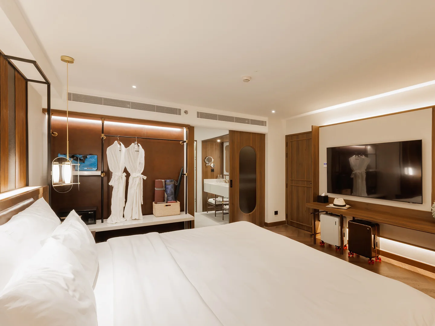 The bedroom of the 62 sqm One-Bedroom King Suite at Public House Bangkok, with the king bed, bathrobes at the open wardrobe and a wall-mounted Smart TV