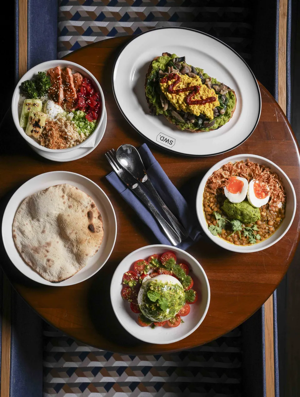 A shared lunch at SWD Bangkok: grain bowls, flatbread and salads on a round table