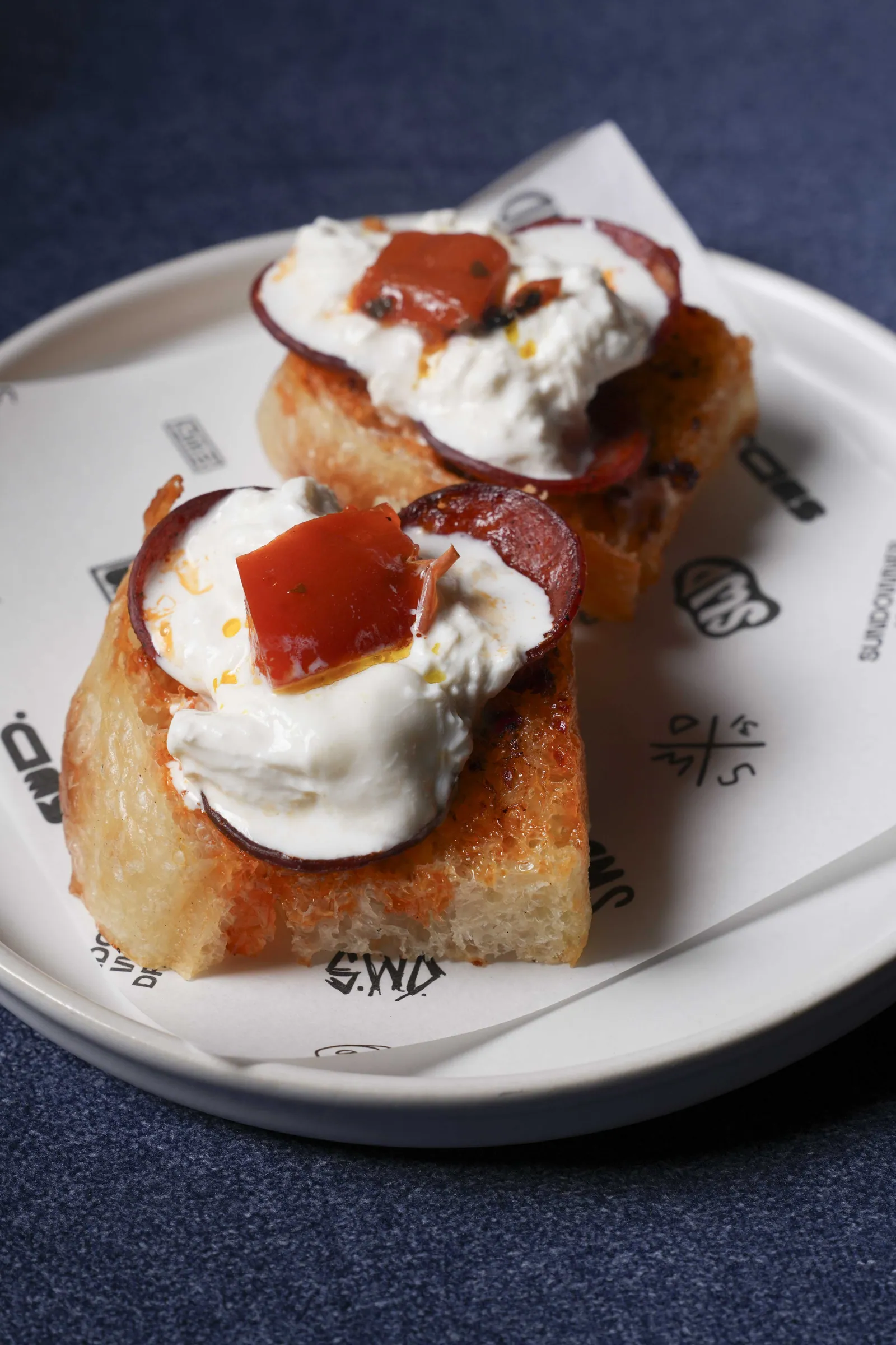 Two slices of focaccia at SWD topped with soft cheese and cured meat, served on SWD paper