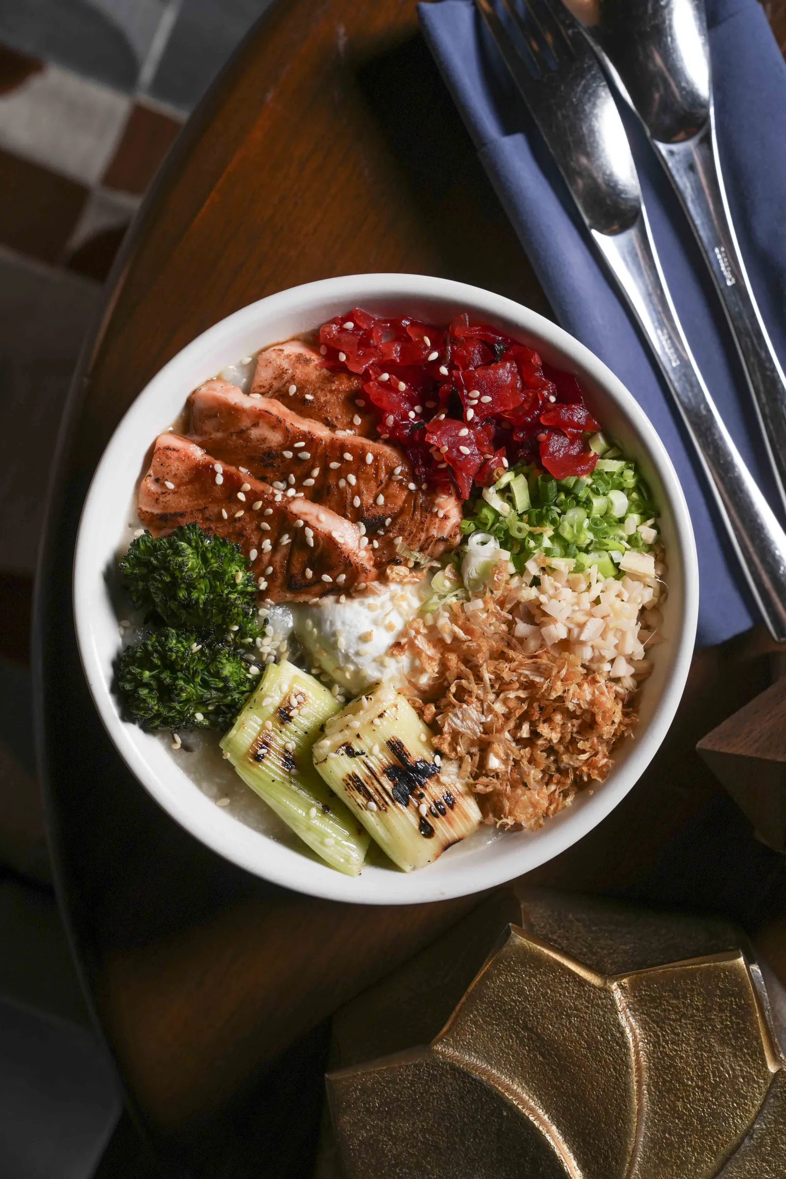 A rice bowl at SWD with salmon, broccoli, grilled leek, spring onion and bonito flakes, on a dark table